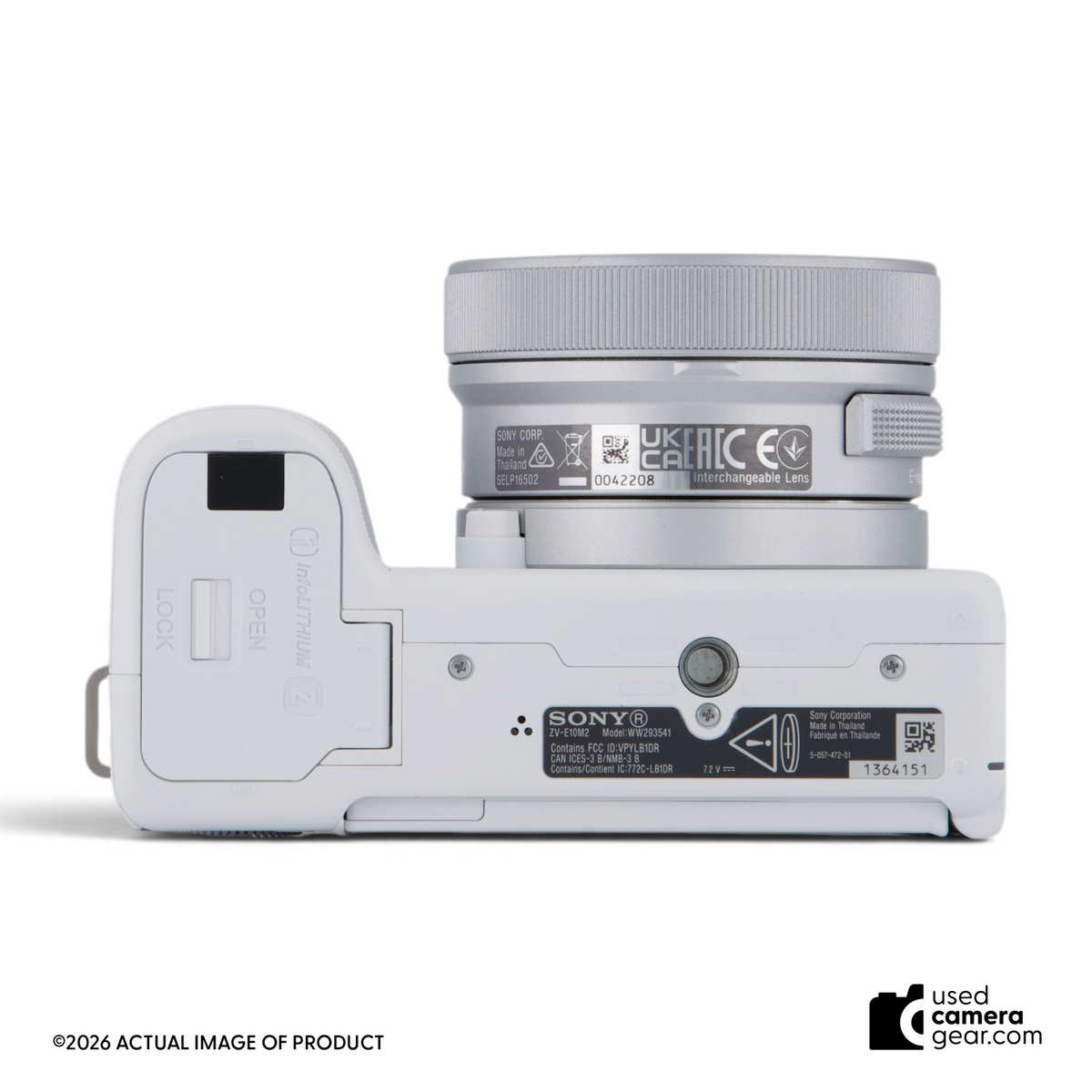 White Sony ZV-E10 II mirrorless camera with 16-50mm lens, bottom view showing battery compartment and tripod mount.