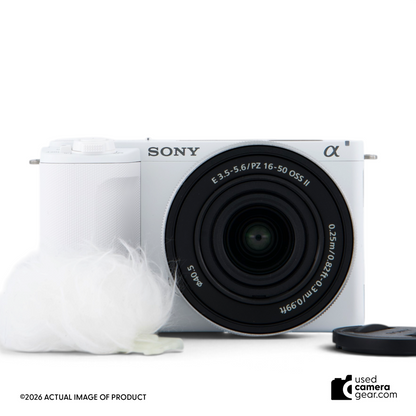 Used Sony ZV-E10 II mirrorless camera in white with 16-50mm power zoom lens and wind muff, front view.